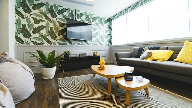 How to improve a room. Interior design. Rug covers all legs of the coffee table in this living room. Wall has a leaf design with a white wall background. Sofa has yellow cushions which pop in the room. 